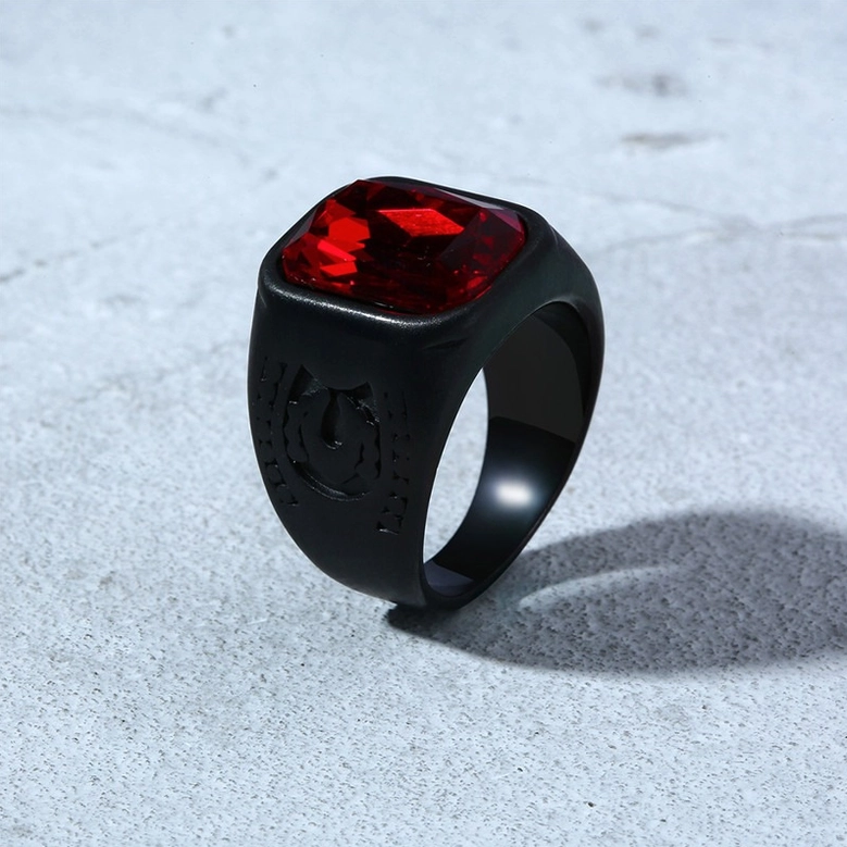 Black stainless steel gothic ring with red gem on gray concrete surface oblique top view embossed patterns