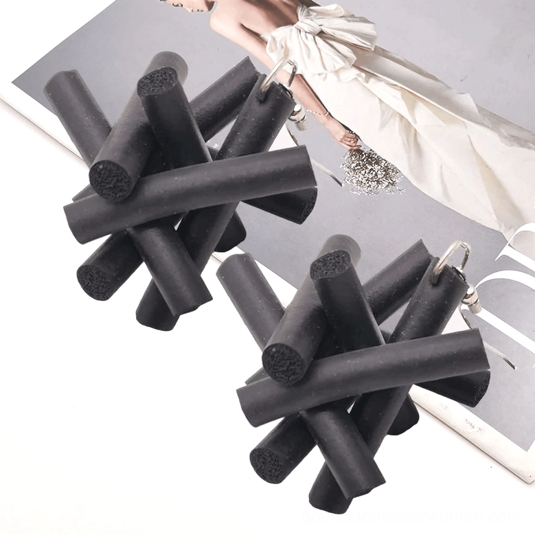 Black rubber crossed-stick drop earrings pair on magazine page background showing punk gothic aesthetic details