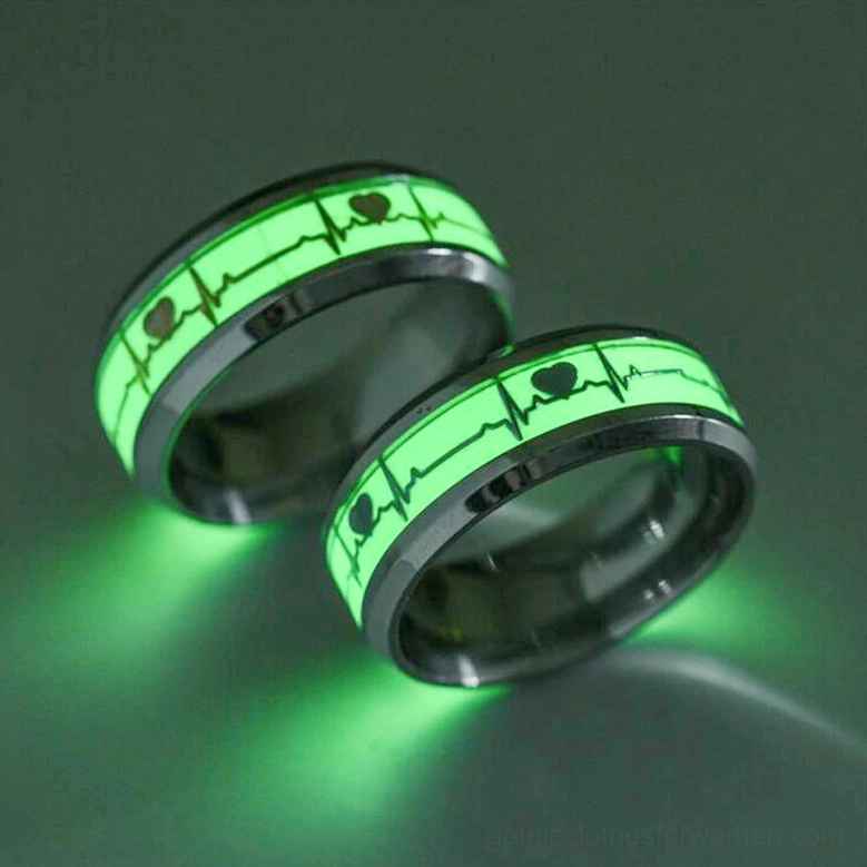 Black stainless steel luminous ECG heartbeat ring pair, dark studio background showing bright green phosphorescent glow