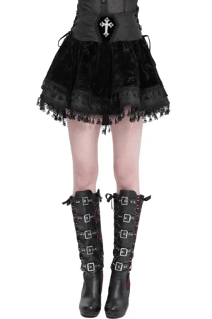 Black velvet gothic mini skirt with embroidered cross waist and lace-up corset front, paired with black buckled knee-high boots, showing front view