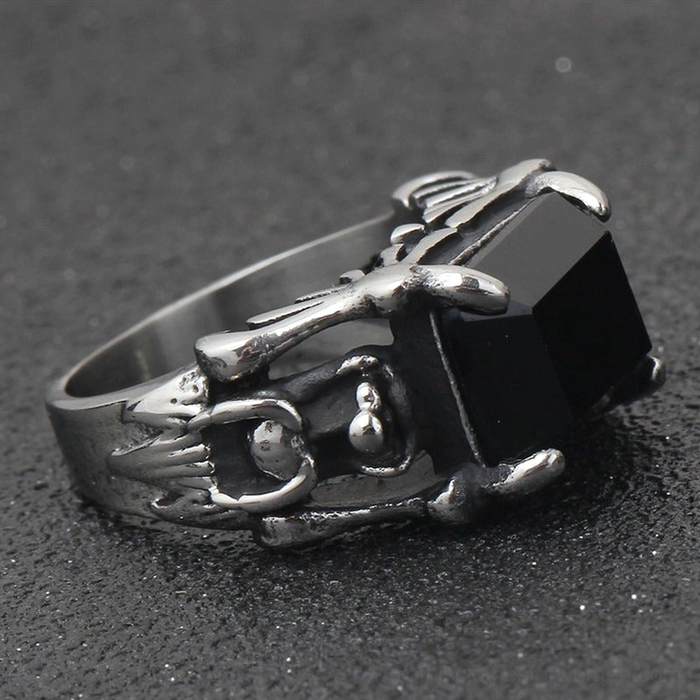 Occult gothic ring side-top angle view displaying aged black silver finish, winged frame details, and square black gemstone on dark textured surface