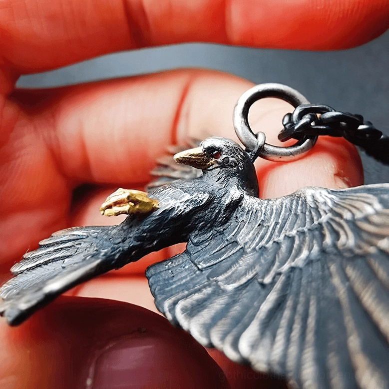 Close-up profile view of gothic crow pendant in hand highlighting dark silver tone and golden bird talons detail