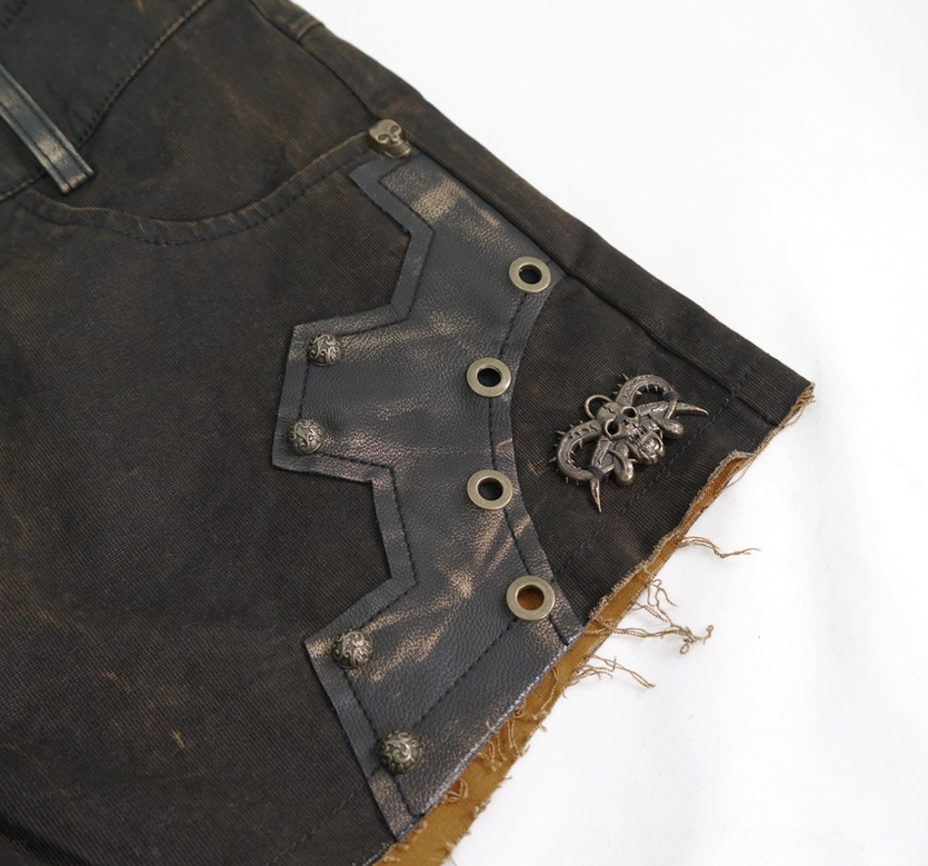 Brown gothic shorts side panel close-up - frayed raw hem, scorpion charm, rivet fasteners