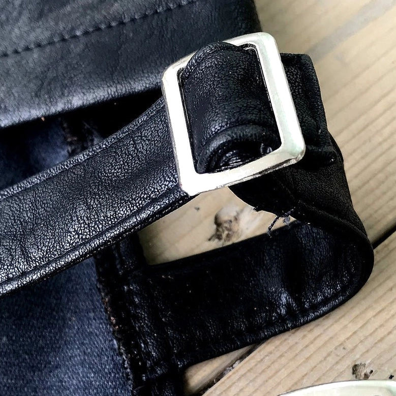 Macro close-up of single adjustable buckle strap on black faux leather shorts with silver hardware