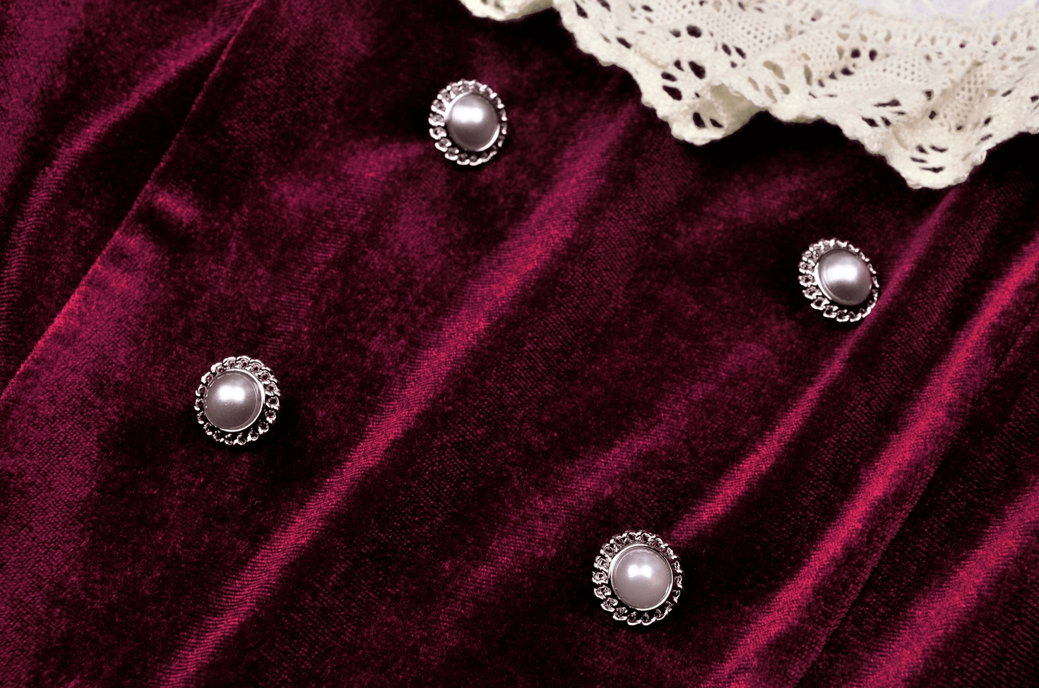 Macro close-up of pearl-inlaid metal buttons on burgundy gothic velvet dress showing craftsmanship detail