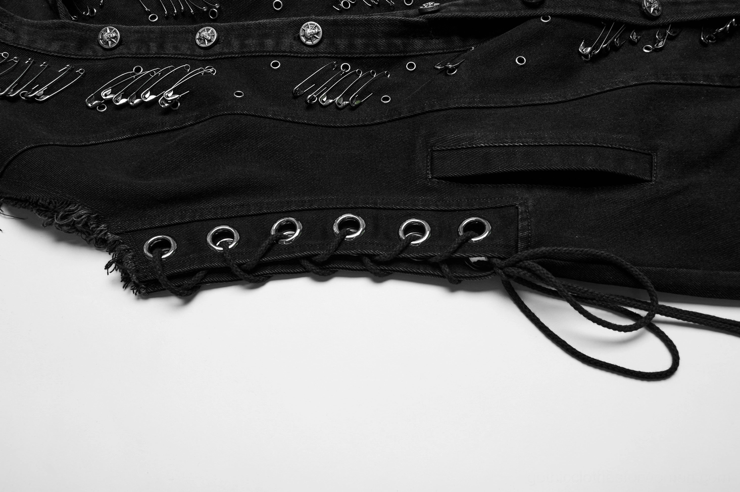 Closeup of denim cape side lace-up detail, metal grommet straps, safety pin decorations and front waist pocket