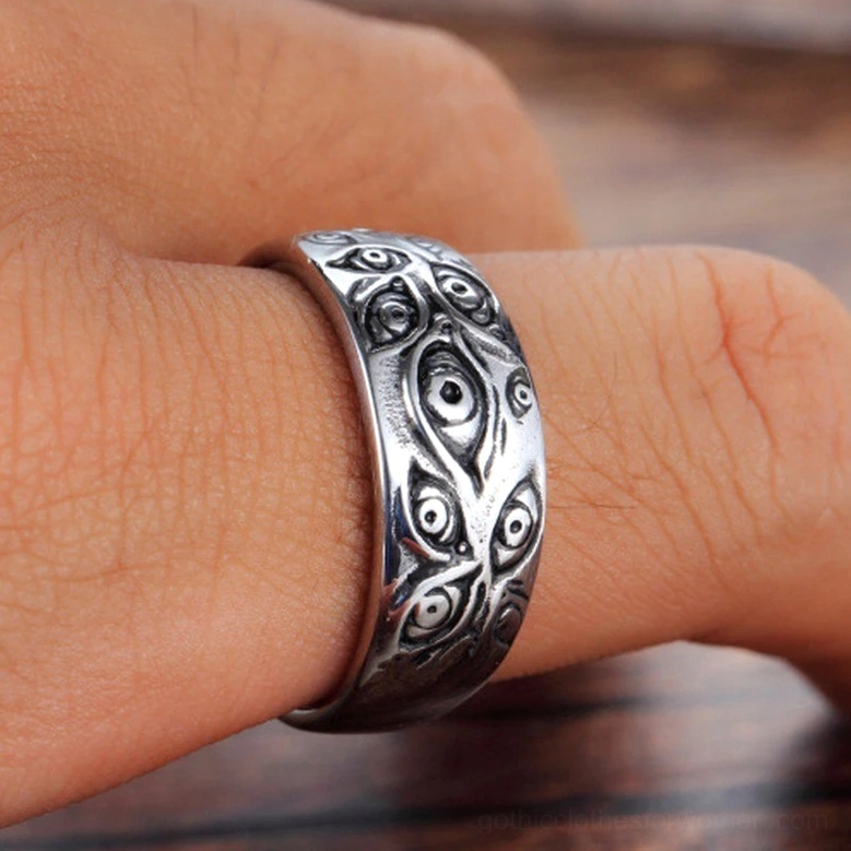 Close-up worn view of carved eyes punk ring on human finger against wooden background showing distressed vintage silver finish and authentic gothic aesthetic