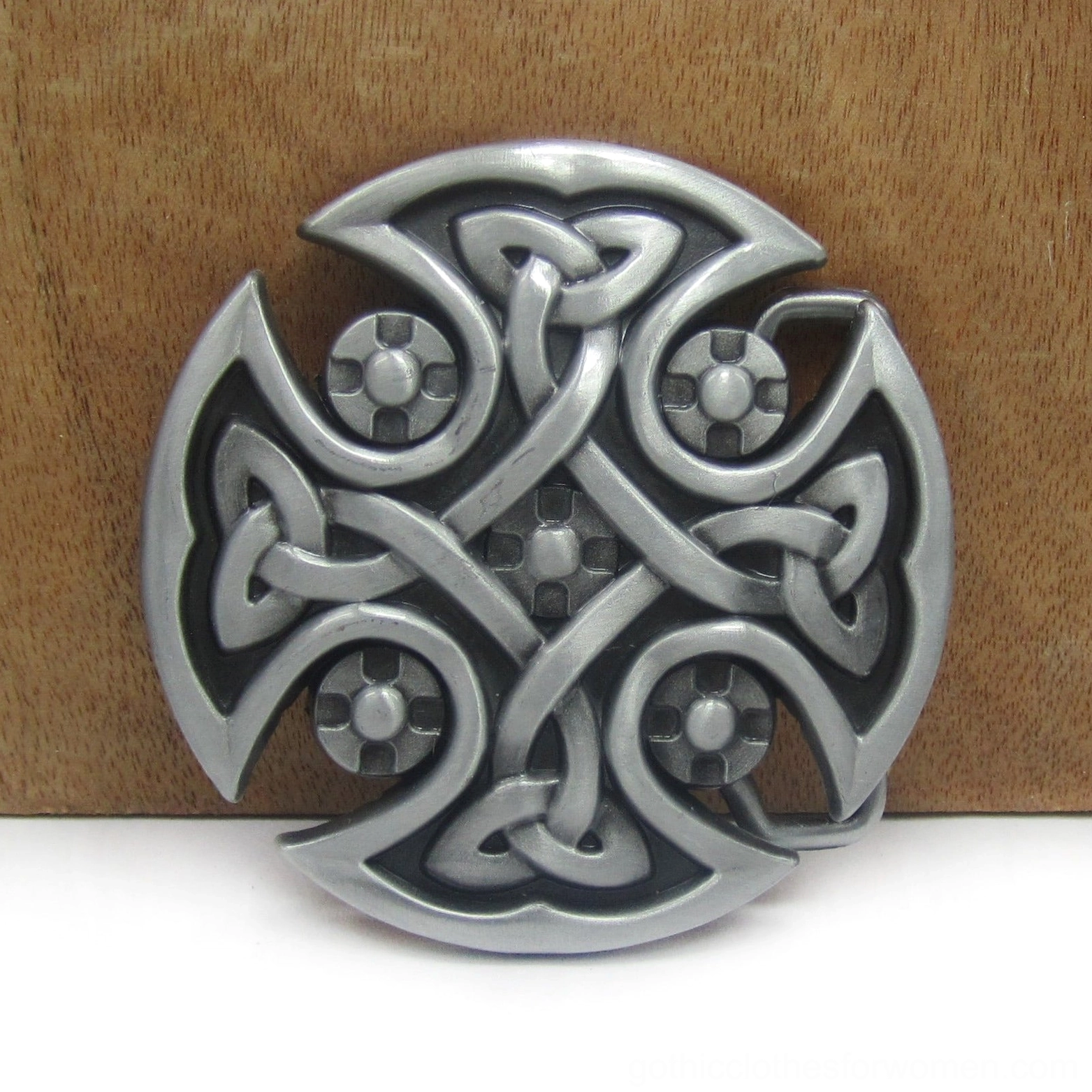 Antique silver Celtic cross buckle on wooden background showing detailed carved cross pattern