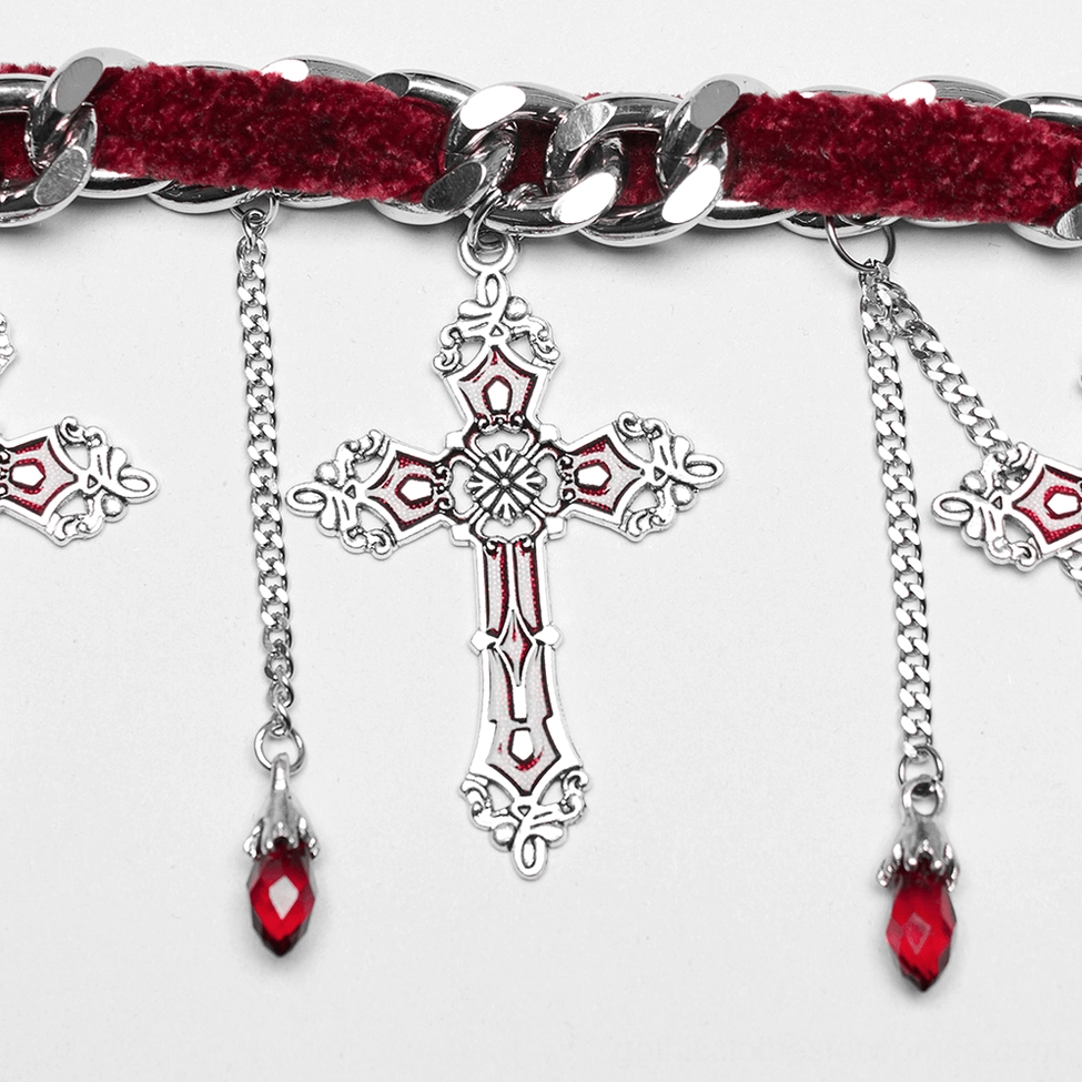 Detailed close-up of engraved silver cross pendant with red enamel detail and red crystal teardrop dangle on chain, macro photography