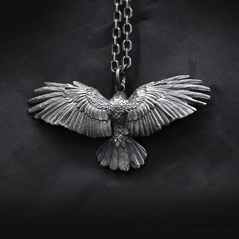 Back flat lay view of blackened silver crow pendant necklace on dark fabric showing intricate carved feather details