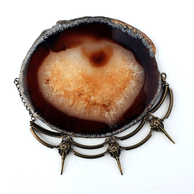 Crow skull charm bracelet displayed with agate stone, top-down view showing multiple bird skull charms in antiqued bronze metal