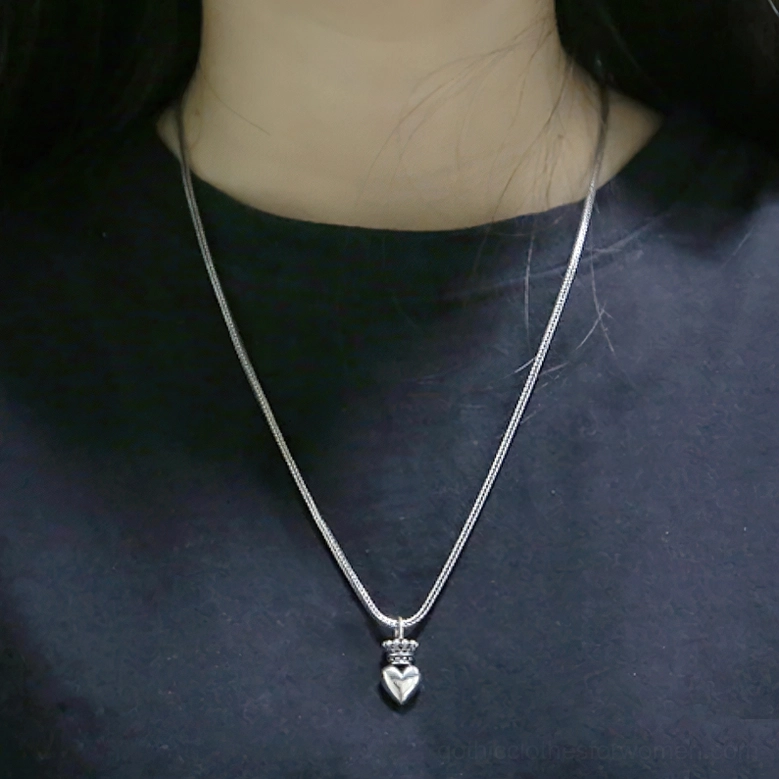 Woman wearing crowned heart gothic necklace, slim silver chain with dark crewneck, casual wear styling