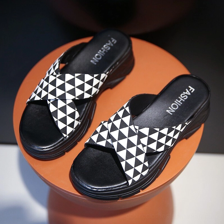Black and white crisscross platform slide sandals with geometric straps and branded insole, top-down front angle view