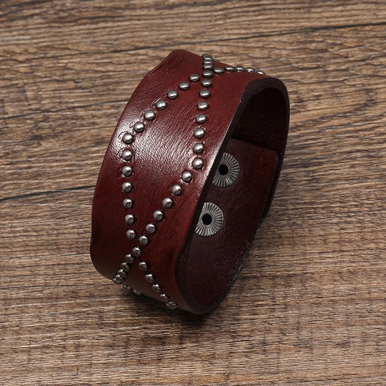 Dark brown leather gothic cuff bracelet with cross rivet embellishment, angled front view on wooden table background
