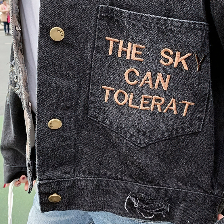 Denim jacket front pocket embroidery details, distressed hem and metal snap closure close-up view