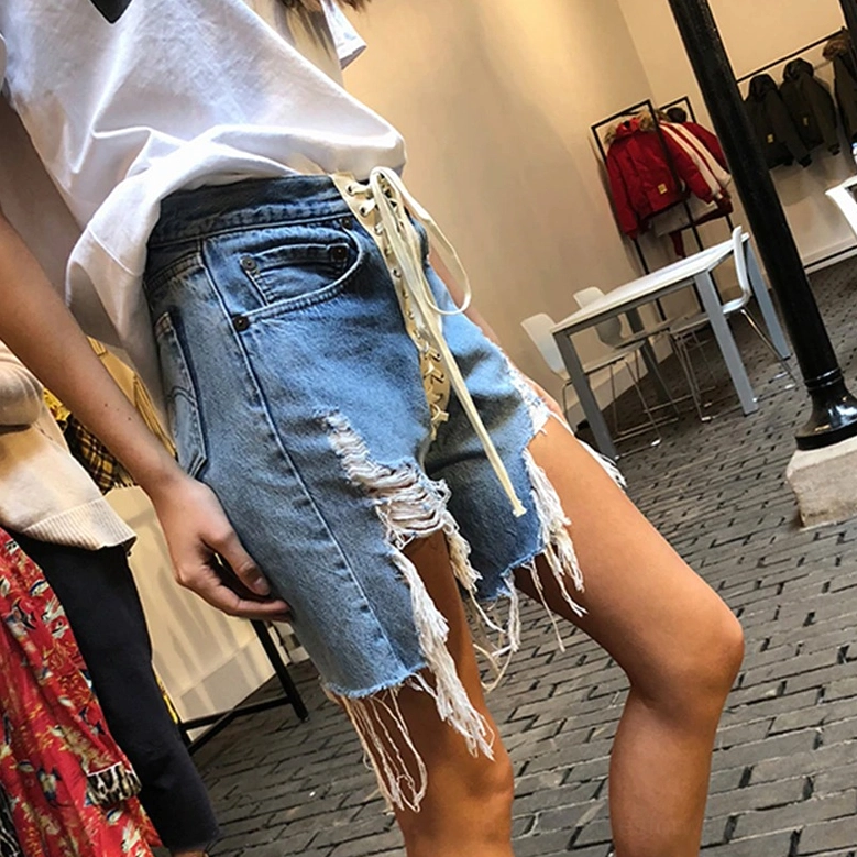 Side rear view of model in light blue distressed denim shorts showing ripped frayed hem and lace-up tie detail
