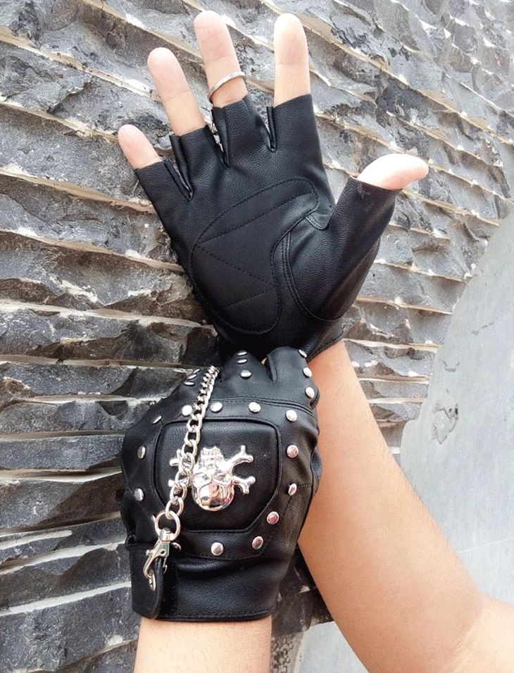 Black faux leather half-finger gloves with prominent metal skull head and rivet embellishments - product photography