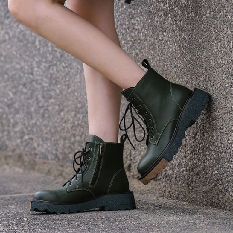 Woman wearing forest green gothic platform ankle boots with side zipper, outdoor concrete wall background, street style demonstration