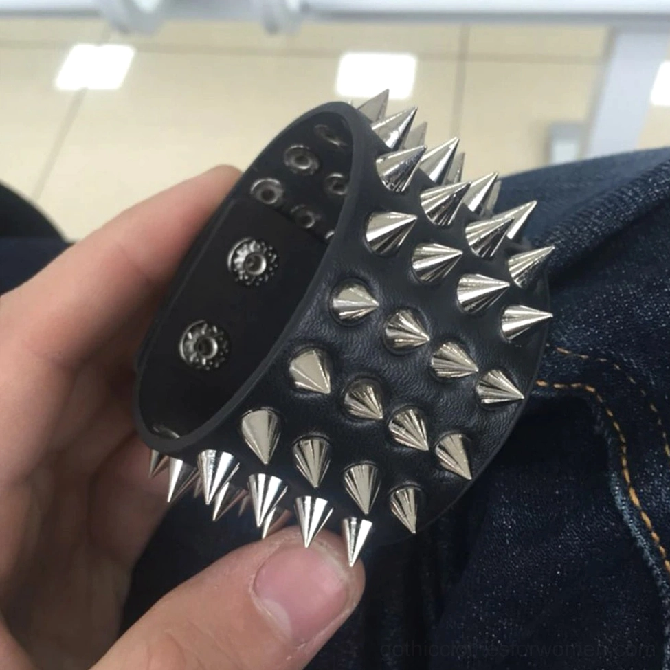 Close-up detail shot of spiked gothic bracelet held in hand showing metal cone spike texture and hidden safety clasp mechanism