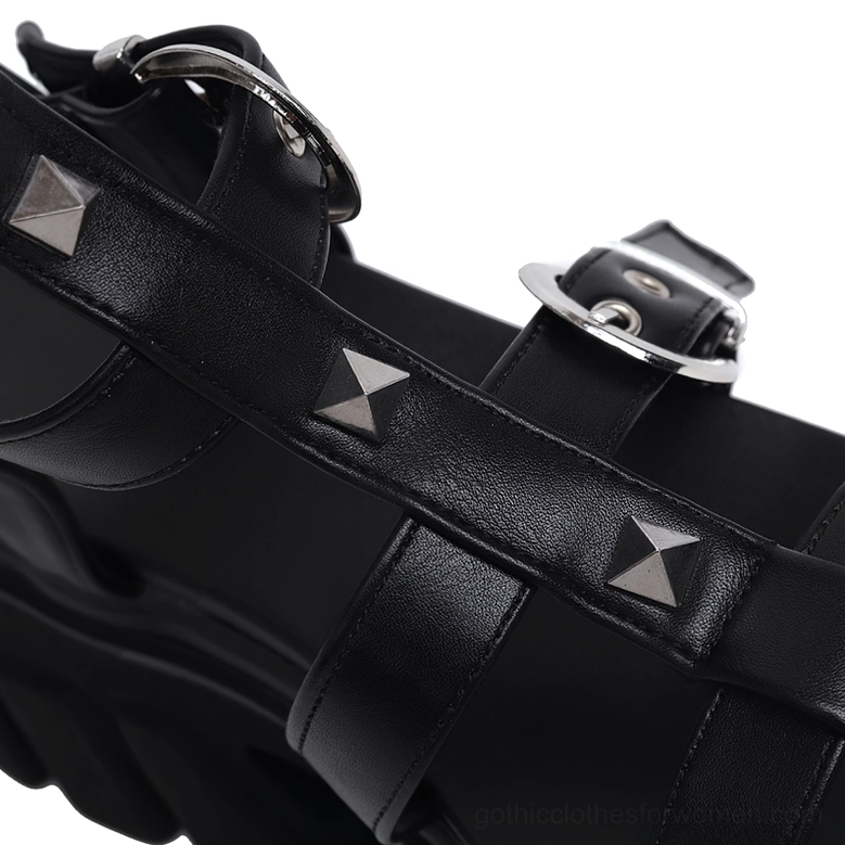 Close-up detail shot of black gladiator sandal hardware, featuring silver pyramid studs, D-ring buckles, and leather construction