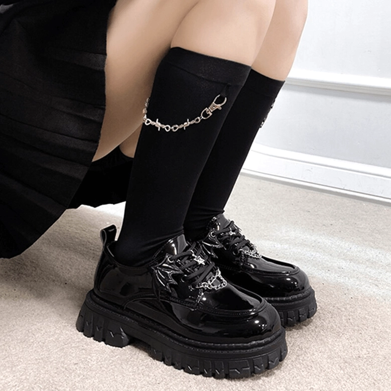 Woman wearing black gothic platform loafers with ankle chain accessory and matching knee-high socks, low side view demonstrating chunky sole