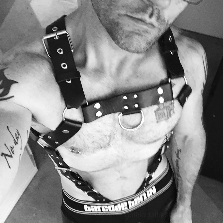 Tattooed model wearing PU leather goth punk body harness on bare chest, gothic style fashion showcase