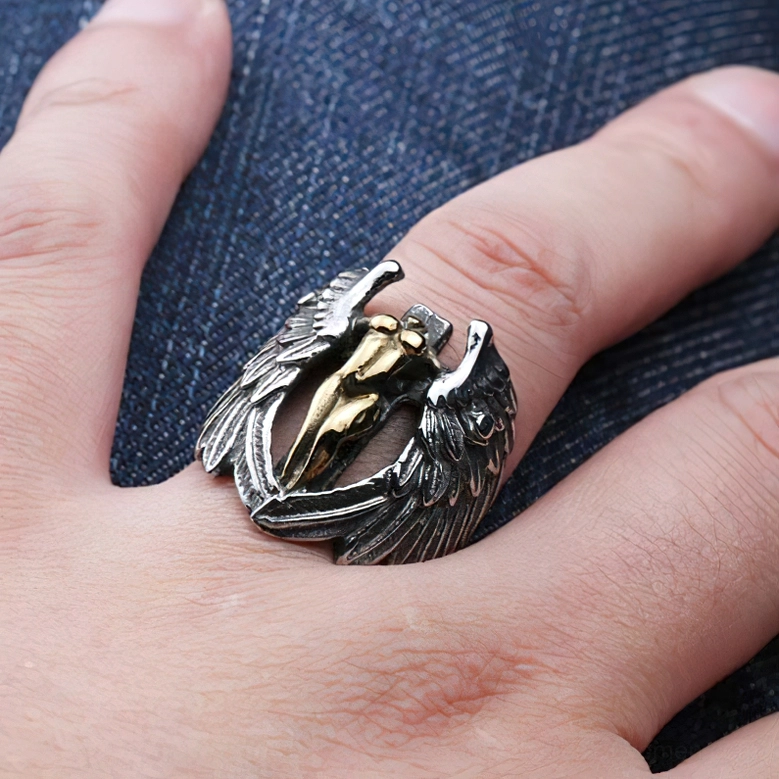 Gothic angel wings two-tone ring worn on index finger with denim background close-up