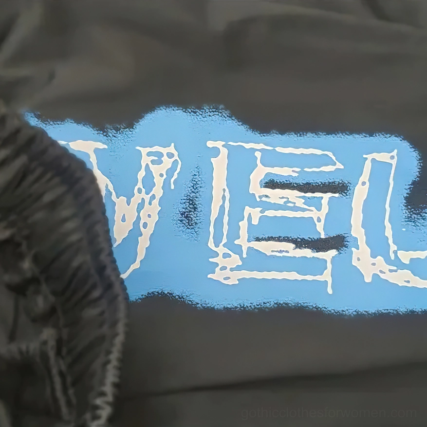 Close-up side view of black gothic anime print jogger pants showing elastic waist edge and partial graffiti design