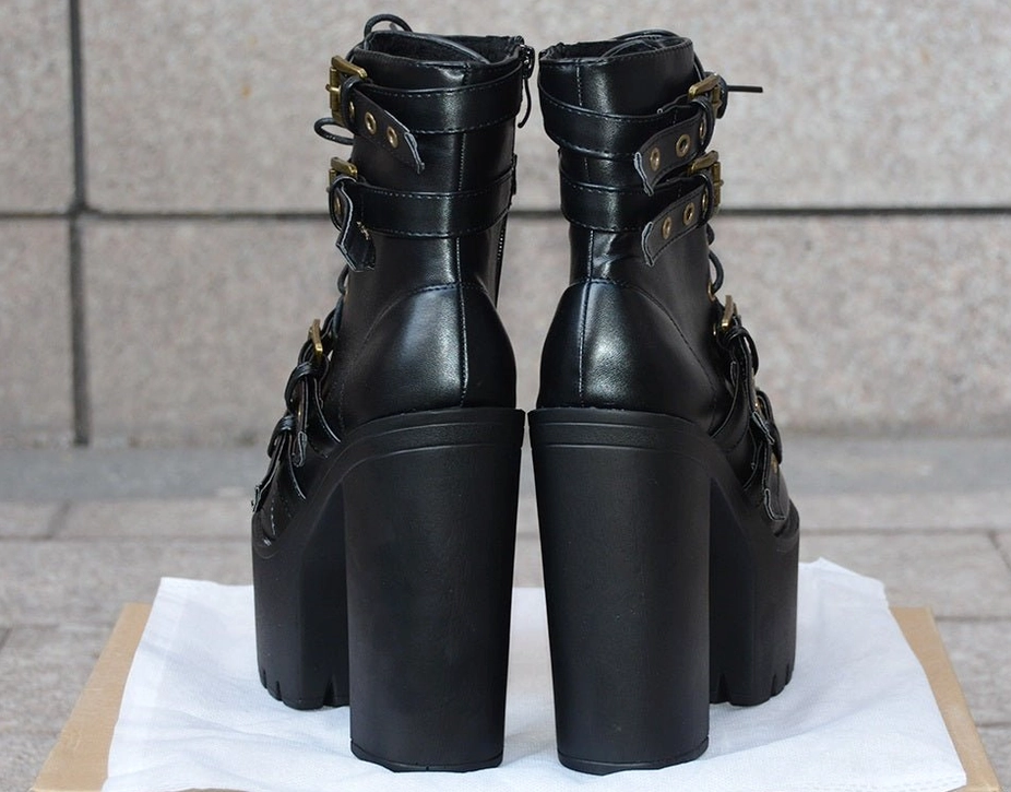 Detailed side profile of gothic ankle boots featuring multiple decorative straps, metal hardware, and substantial heel-to-platform geometry