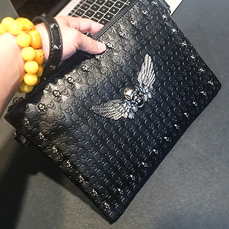 Close-up of black gothic handbag showing metal skull-wing centerpiece and studded leather edges