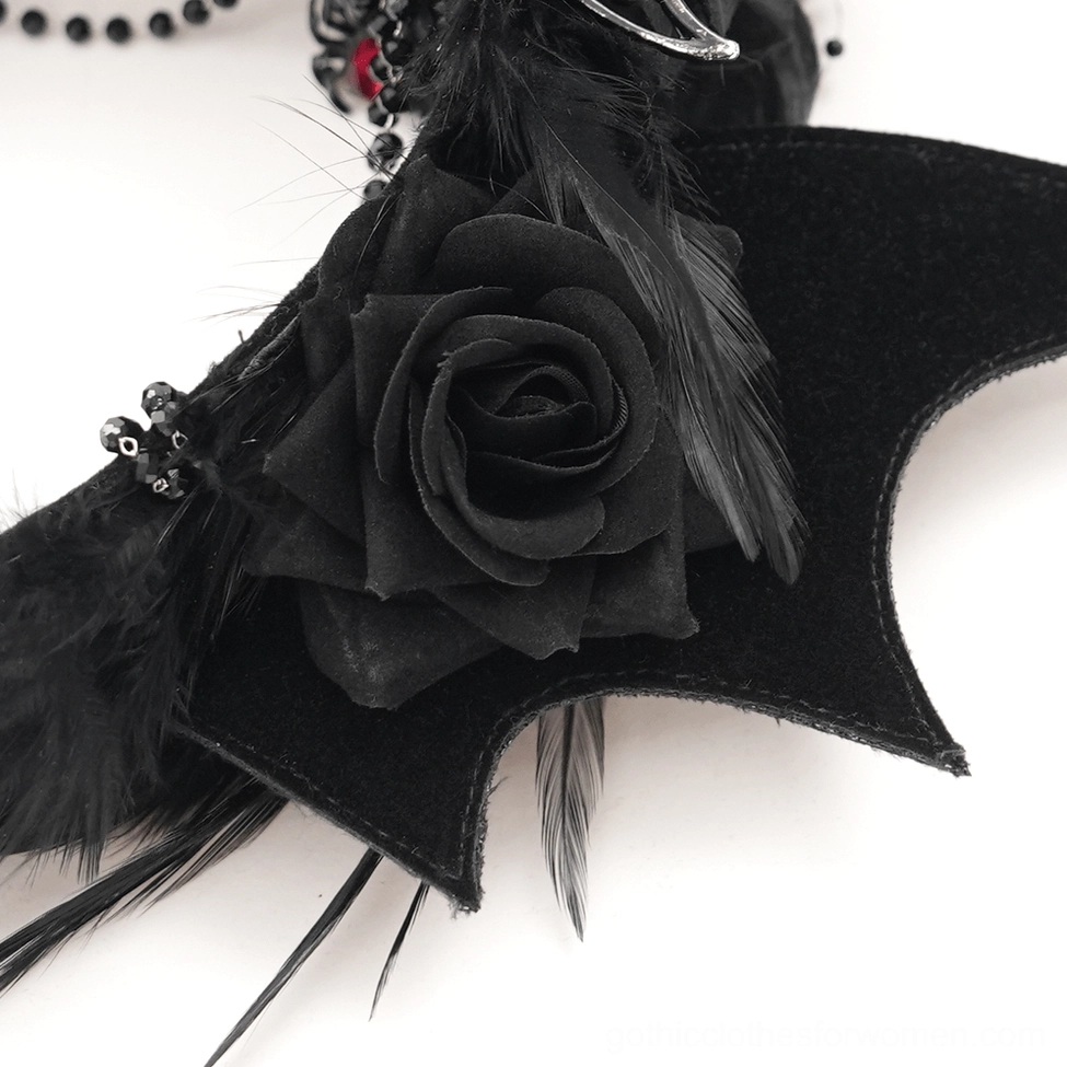 Macro close-up of gothic bat crown detail showing black velvet fabric rose, feather, and bead accents