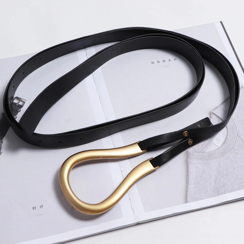Black gothic belt coiled flat lay side angle on fashion magazine, gold metal buckle visible, showing material texture and premium construction details
