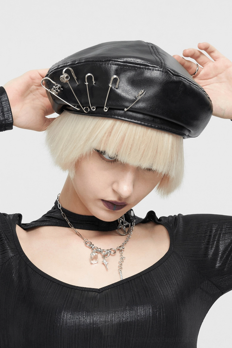 Front low angle of model adjusting black leather gothic beret with hands, showing multiple safety pins and layered gothic necklaces