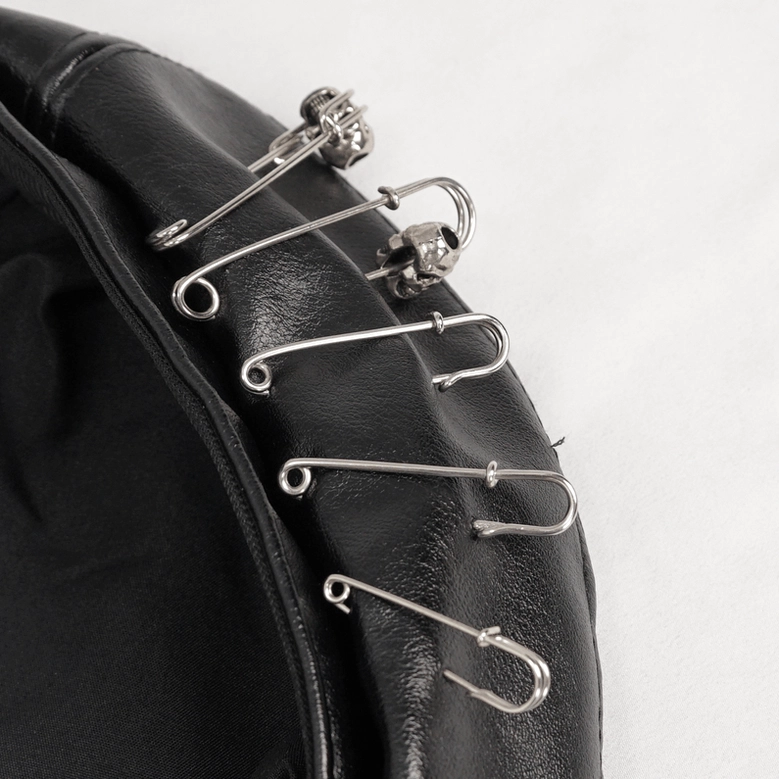 Detail view of black faux leather gothic beret highlighting safety pin arrangement and industrial elements