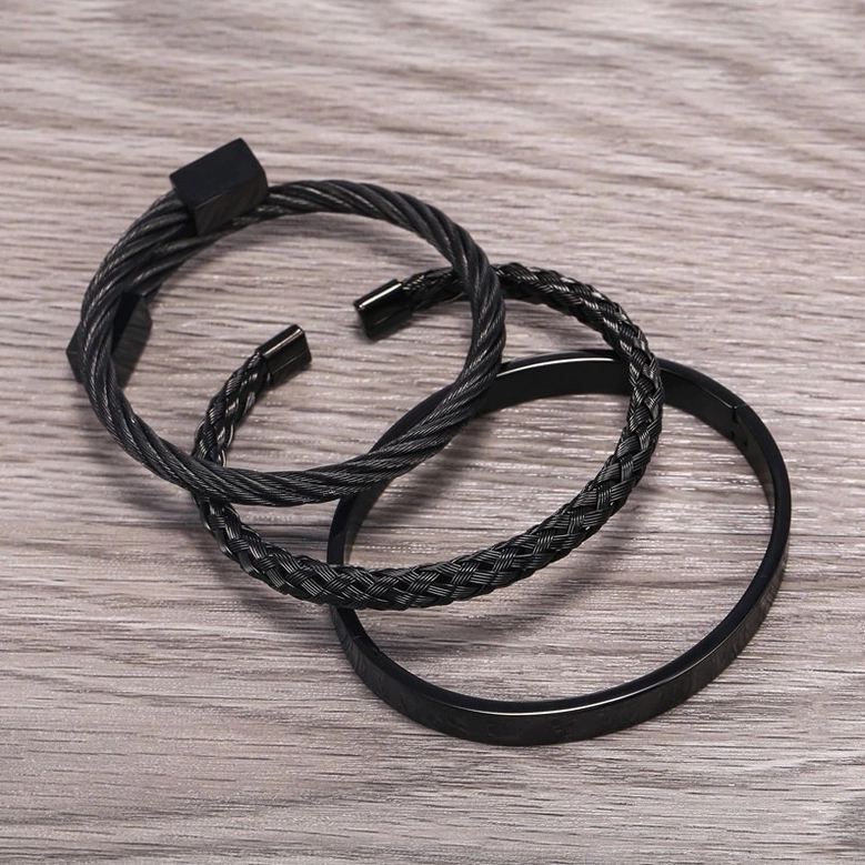 Angled view of black mixed-texture 3-piece stainless steel gothic bangle set on wooden surface, punk-inspired dark metal bracelet collection