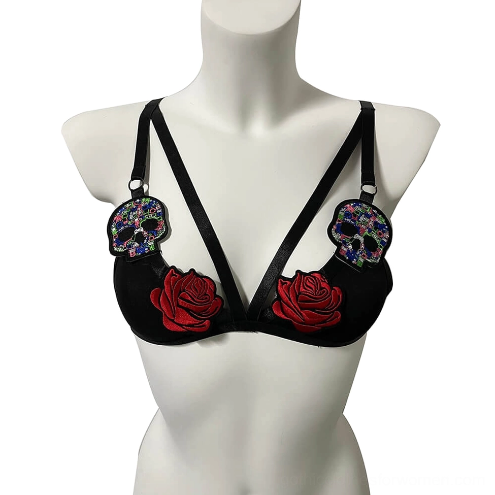 Black gothic bralette with embroidered red roses and colorful sugar skull patches, front view with adjustable straps on white background