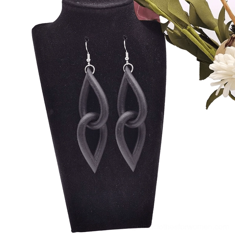 Neo-gothic black dangle earrings on black jewelry display bust with artificial flowers, demonstrating twisted interlocking link construction and matte black finish