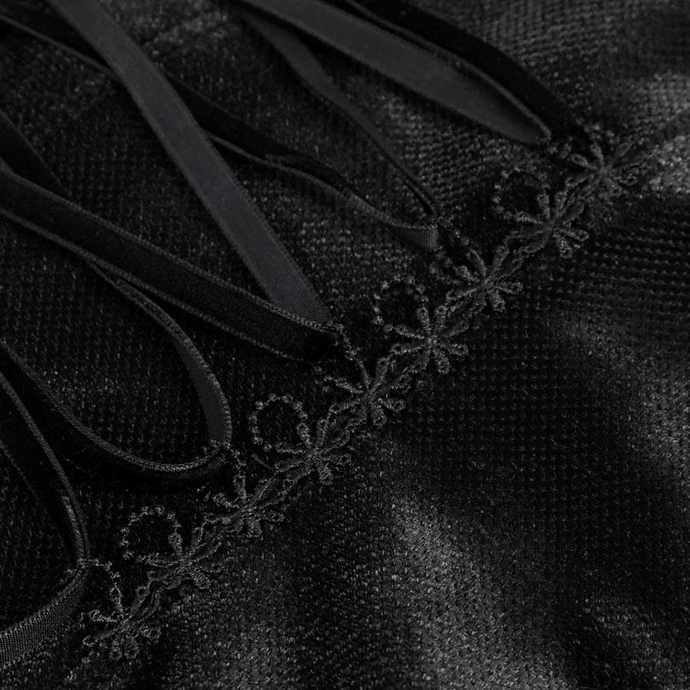 Ornamental detail of black gothic blouse showcasing gemstone button embellishment and velvet fabric surface texture