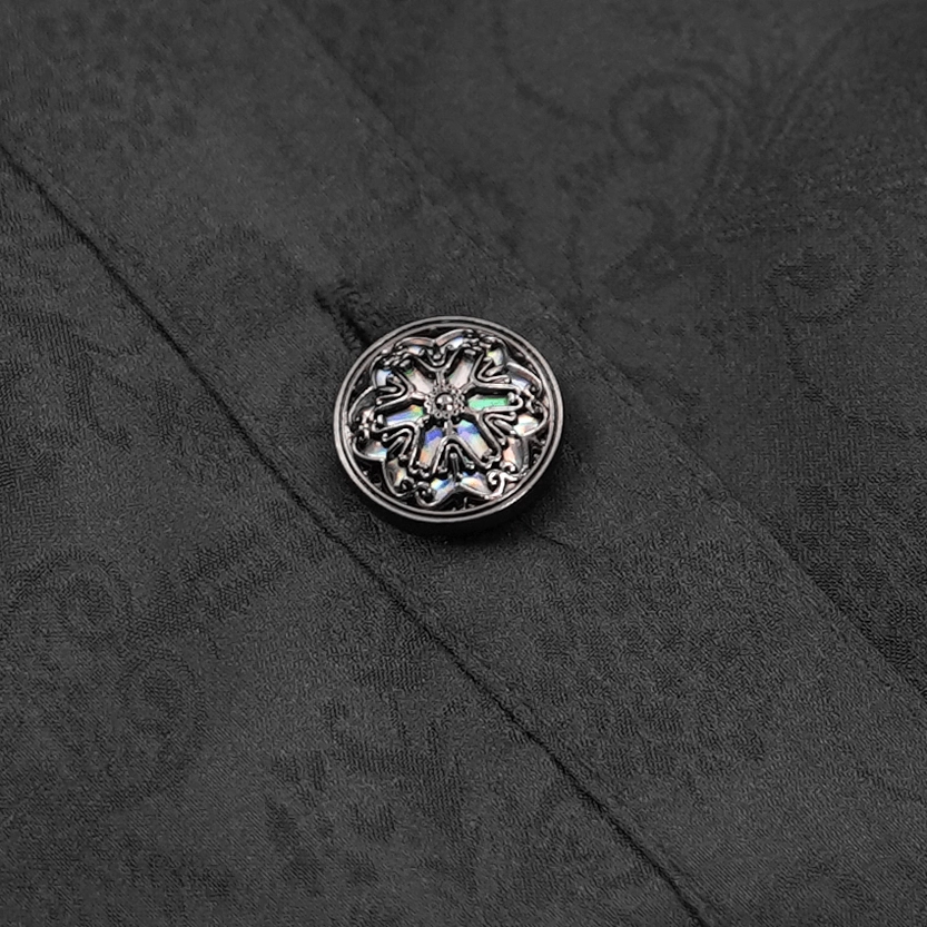 Embossed metal button detail on Victorian gothic blouse with iridescent inlay against damask jacquard fabric background