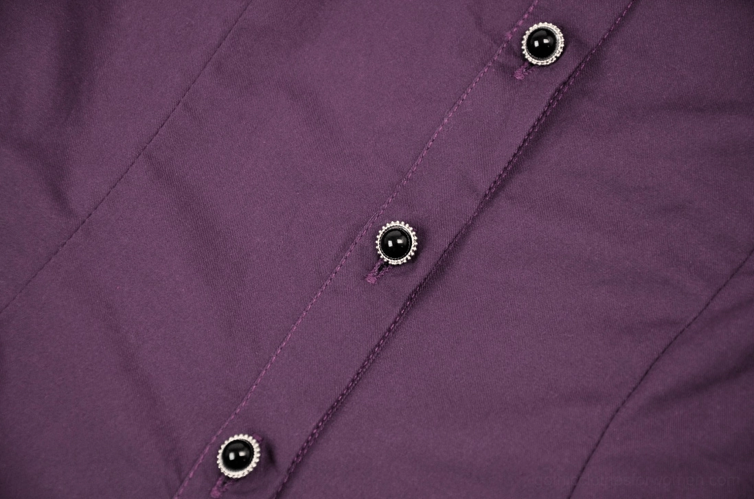 Close-up detail of silver-rimmed black buttons on purple gothic blouse fabric background