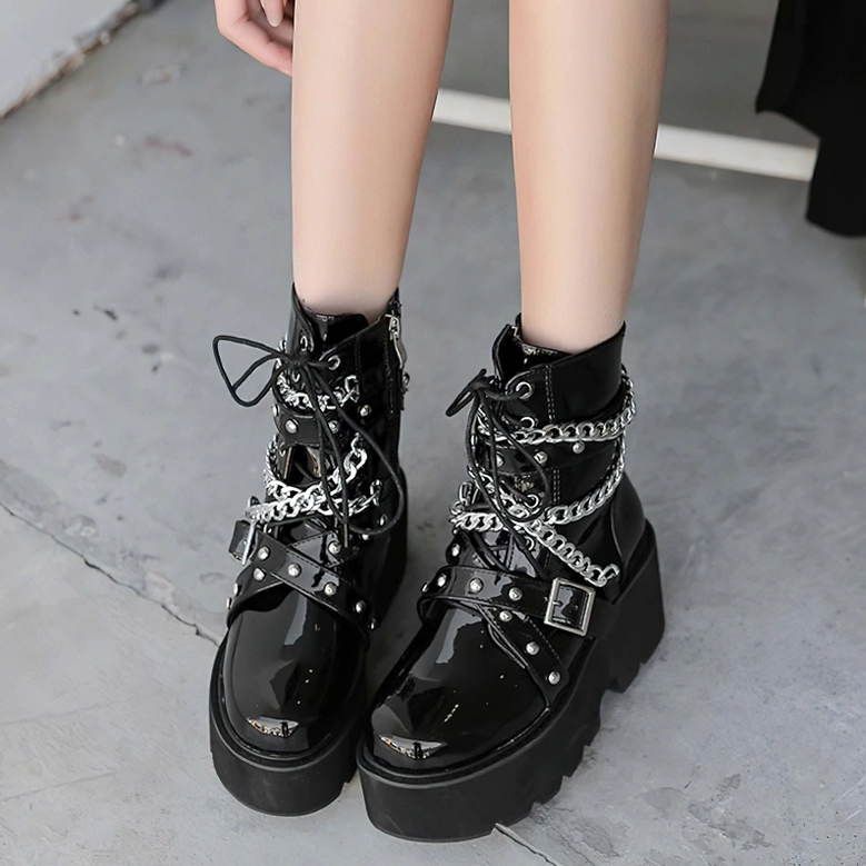 Woman modeling black gothic ankle boots with rivet decorations on concrete ground, front low view punk rock aesthetic