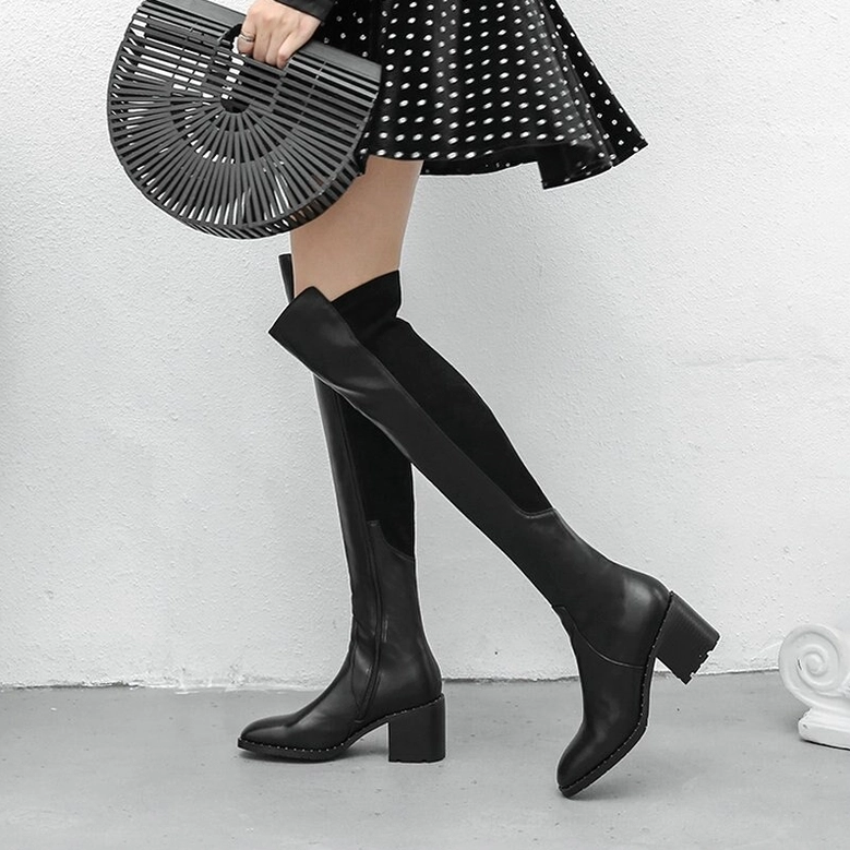 Woman styling black leather over-the-knee boots with polka dot dress and chunky block heel in minimalist setting