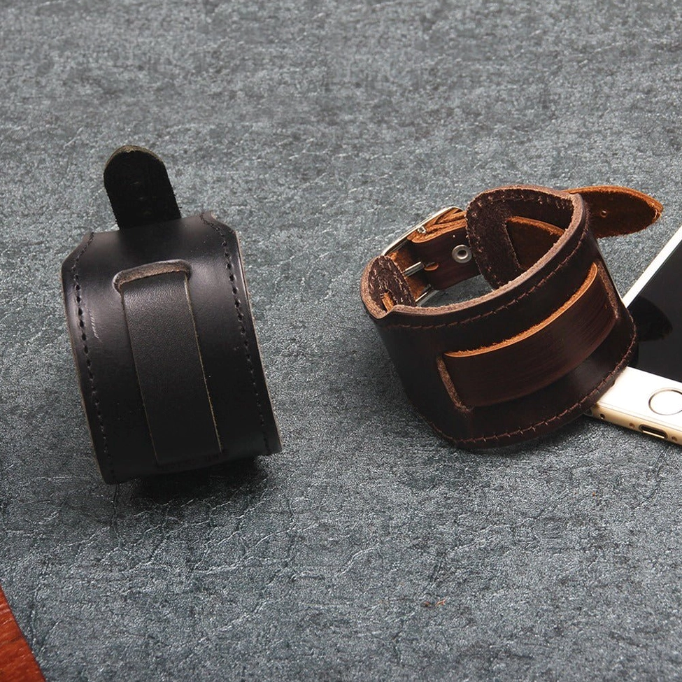 Two-color leather gothic bracelets arranged on dark gray tabletop, overhead perspective displaying buckle mechanisms and alternative styling context