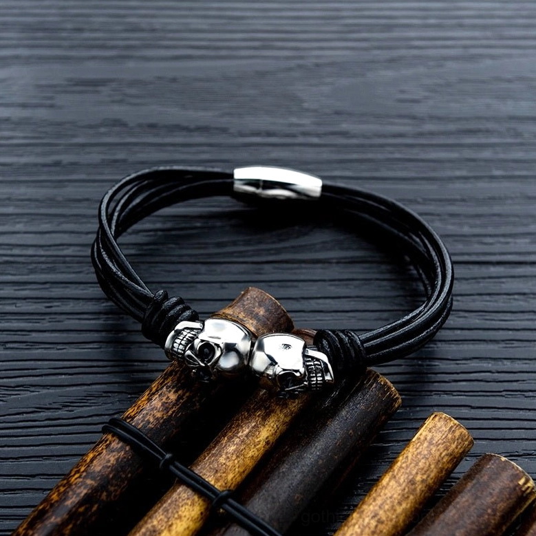 Black gothic skull bracelet displayed on wooden table showing multi-strand cord and metal charm details