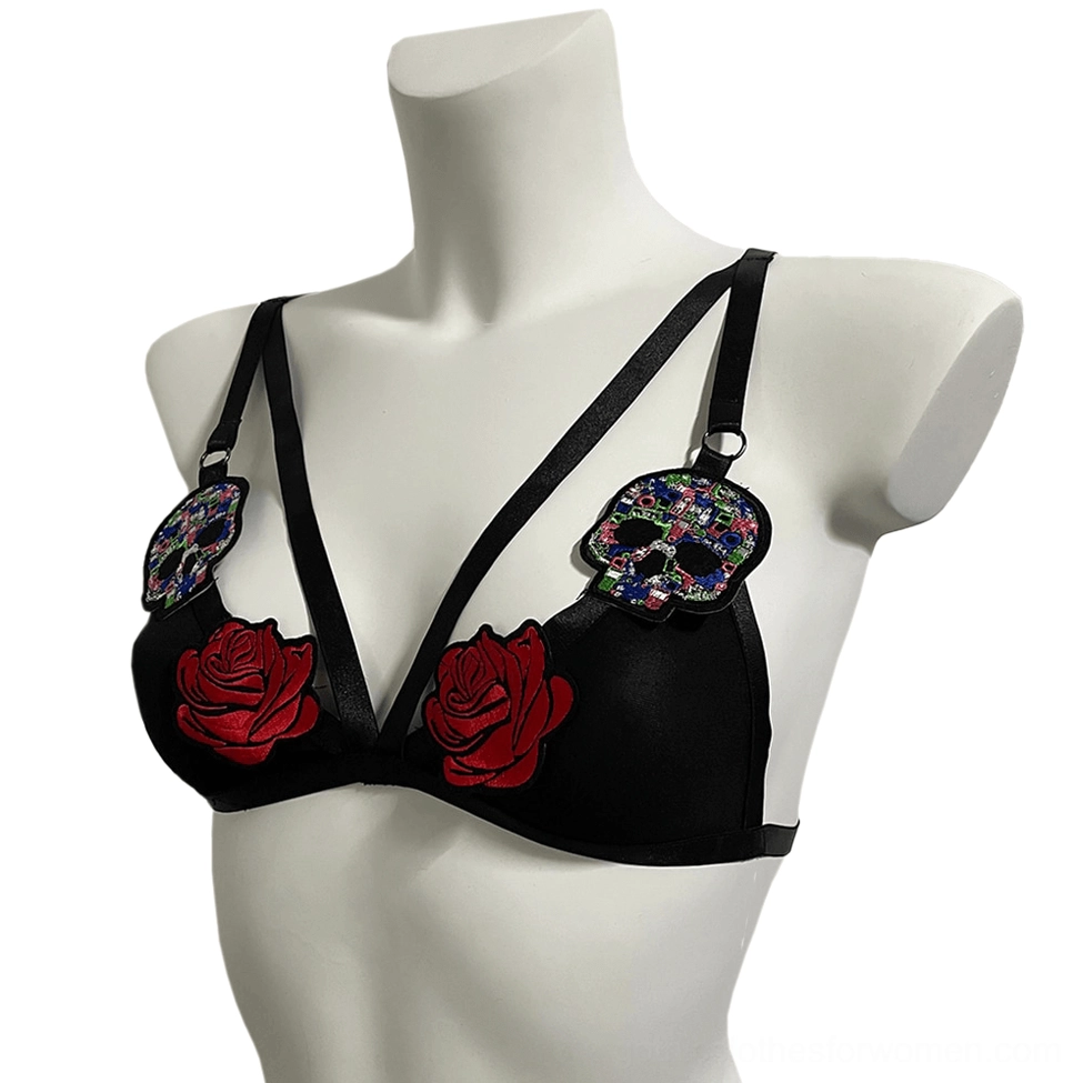 Black romantic gothic bralette with embroidered red roses and skull patches, three-quarter left front view showing adjustable strap details
