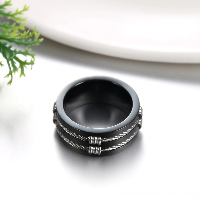 Overhead top-down view of black gothic cable ring on studio surface with green decor, clearly showing polished inner band and embedded twisted wire design