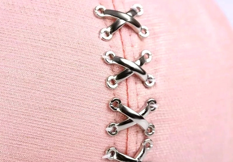 Close-up detail of silver metal cross ring fasteners on pink fabric baseball cap