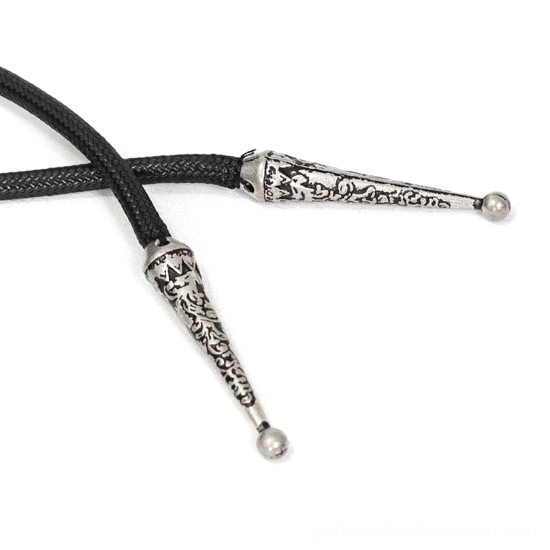 Close-up detail of gothic cape drawstring accessory with carved metal cord ends and black braided rope