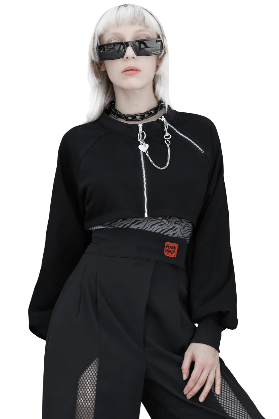 Black chain-adorned crop jacket with dual front zippers and heart charm detail, displayed on platinum blonde model in studio setting