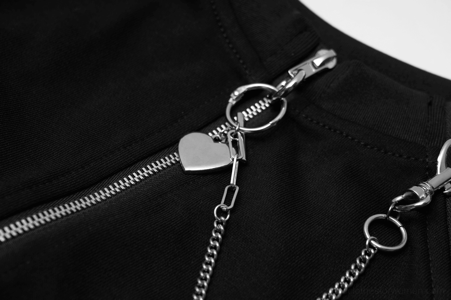 Macro detail of silver chain with heart charm attached to main zipper slider on black knit fabric